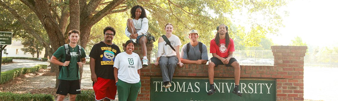 photo of students posed around a Thomas University sign